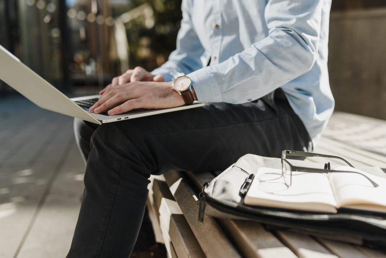 Man sitting on bench outside working on laptop